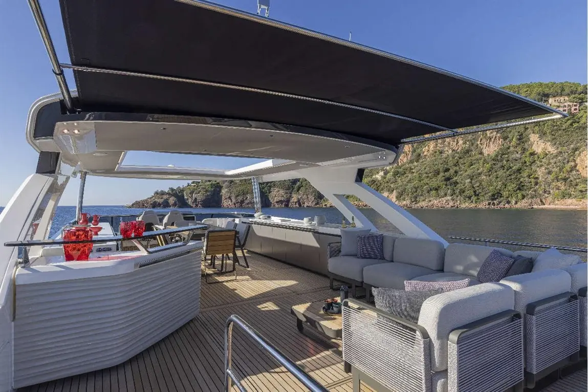 Luxurious yacht deck featuring a seating area, bar, and stunning coastal views under a shaded canopy.